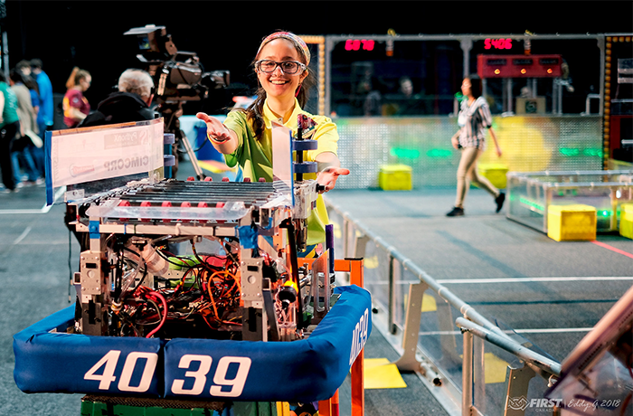 Image of girl smiling and presenting a robot on display.
